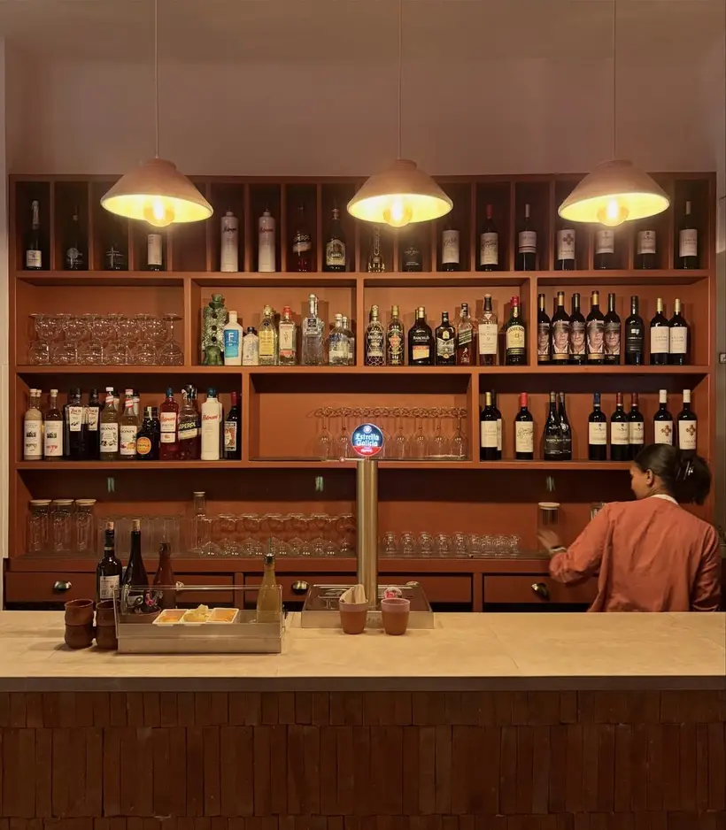 La barra de La inTrépida, con estanterías de madera llenas de botellas y tres lámparas encendidas
