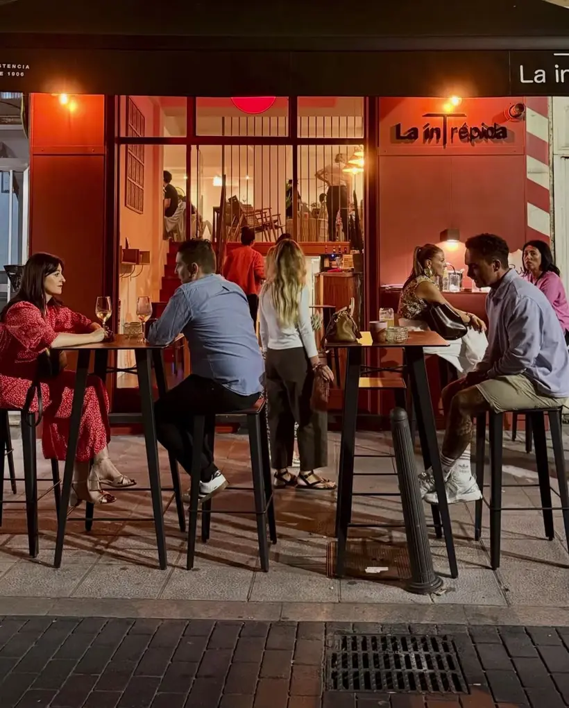 La terraza de La inTrépida de noche, con gente en las mesas altas frente a la fachada roja